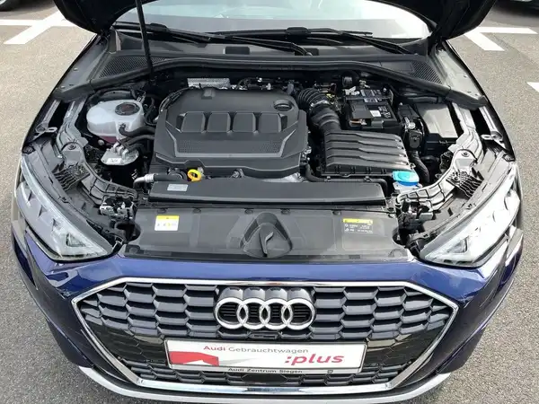 Das Bild zeigt den Motorraum eines blauen AUDI A3 SPORTBACK aus der Frontansicht. Im Bild ist ein Händlerlelogo mit der Aufschrift 'plus' zu sehen.
