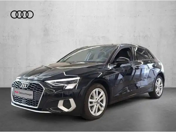 Das Bild zeigt einen schwarzen AUDI A3 SPORTBACK von der Seite. Im Hintergrund ist ein grauer Wandanstrich zu sehen, und es gibt ein Händlerlogo oben im Bild.