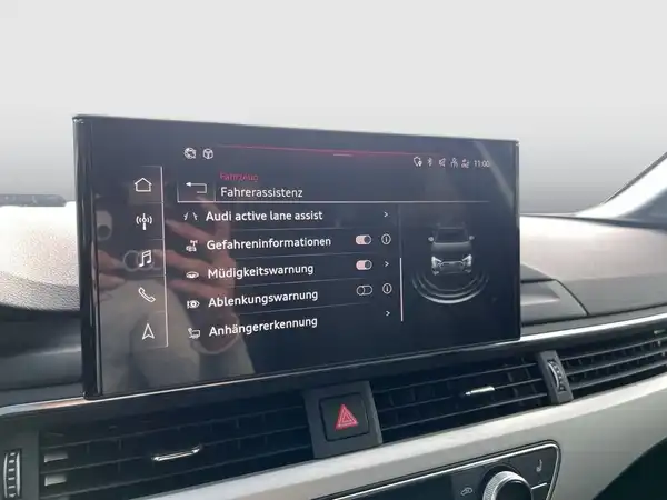 Innenaufnahme des Audi A4 Avant mit Blick auf das Navigationsdisplay, das verschiedene Funktionen wie Fahrerassistenz und Gefahreninformationen anzeigt. Das Interieur ist schwarz.