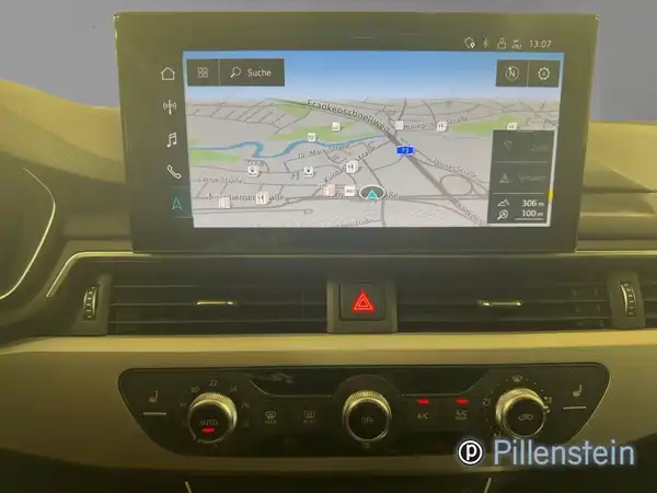 Die Aufnahme zeigt das Innenleben eines AUDI A4 AVANT mit einem Navigationssystem auf dem Bildschirm und Kontrolltasten darunter. Der Innenraum ist schwarz und es befindet sich ein Händlerlogo im Bild.