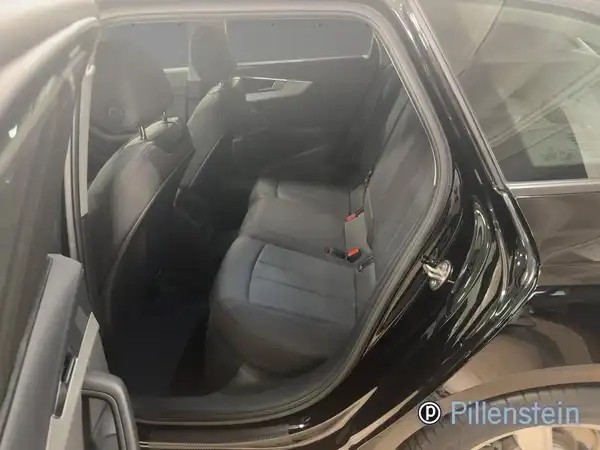 Eine Innenaufnahme des Audi A4 Avant, die Rückbank zeigt. Das Fahrzeug hat eine schwarze Außenfarbe und das Interieur ist dunkelgrau. Zusätzlich ist ein Händlerlogo zu sehen.