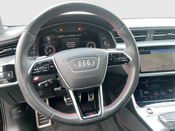 Innenaufnahme eines Audi A6 mit einem sportlichen Lenkrad in Schwarz und roten Akzenten. Das Armaturenbrett und das Infotainment-System sind sichtbar.