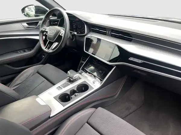 Das Bild zeigt den Innenraum eines Audi A6, mit einem schwarzen Interieur und roten Akzenten.