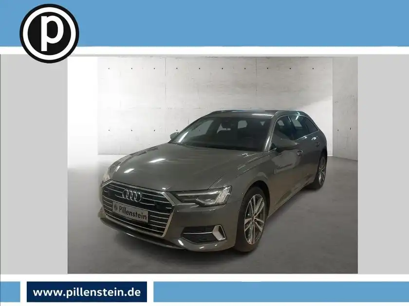 Eine frontale Aufnahme eines grauen Audi A6 Avant in einem Ausstellungsraum, mit einem Händlerlogo in der oberen linken Ecke.