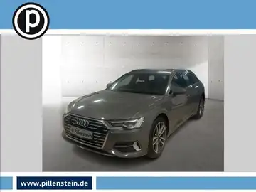 Eine frontale Aufnahme eines grauen Audi A6 Avant in einem Ausstellungsraum, mit einem Händlerlogo in der oberen linken Ecke.