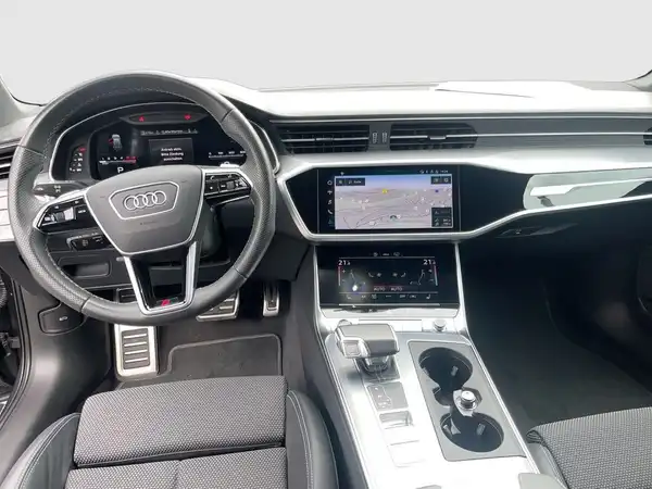 Das Bild zeigt das Innere eines Audi A6 Avant mit einem schwarzen Interieur. Es ist eine Aufnahme des Fahrerbereichs, einschließlich des Armaturenbretts und Navigationssystems.
