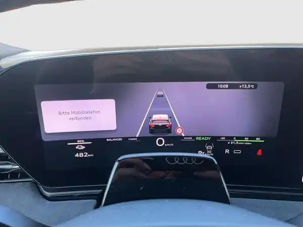 Das Bild zeigt das Innenleben des Audi A6 Avant E-Tron mit einem digitalen Armaturenbrett. Die Hauptfarbe des Interieurs ist schwarz. Es gibt markante Texteinblendungen, die Anweisungen geben.