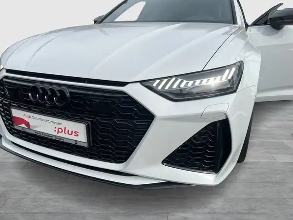 Das Bild zeigt einen weißen AUDI RS6 AVANT, aufgenommen von vorne. Das Händlerschild ist sichtbar und es gibt markante Texteinblendungen.