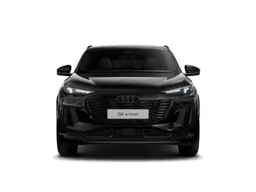 Das Bild zeigt einen schwarzen AUDI Q6 e-tron, aufgenommen von vorne. Es sind markante Texteinblendungen zu sehen.