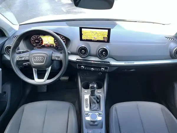Eine Innenaufnahme des Audi Q2 mit schwarzem Interieur und markanten Texteinblendungen auf dem Bildschirm.