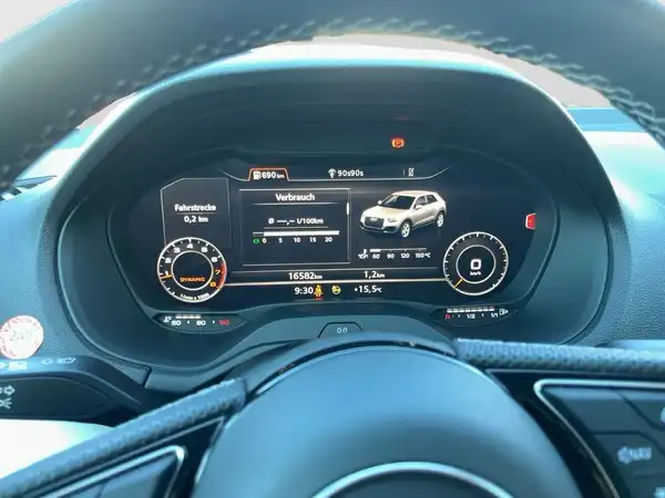 Das Bild zeigt das Interieur eines AUDI Q2, insbesondere das digitale Cockpit. Das Display zeigt Informationen wie Verbrauch und Fahrtüverlauf. Das Interieur ist schwarz.