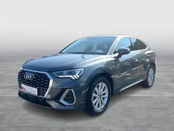 Das Bild zeigt einen AUDI Q3 Sportback in grau, aufgenommen von der Seite. Es enthält das Händlerlogo und einige markante Texteinblendungen.