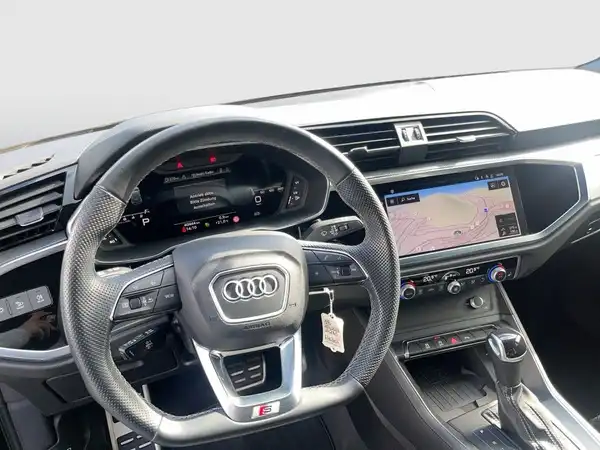 Eine Innenaufnahme des Audi Q3, zeigt das Lenkrad und das Navigationsdisplay. Das Interieur ist schwarz.