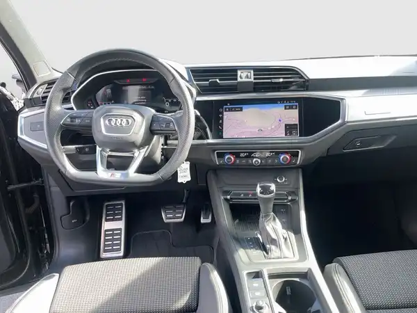 Das Bild zeigt das Innere eines AUDI Q3 mit einem schwarzen Interieur und einem Navigationsgerät auf dem Bildschirm.