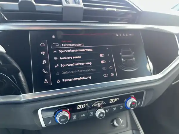 Das Bild zeigt das Innere eines AUDI Q3 mit einem modernen Armaturenbrett und einem Bildschirm, der Fahrerassistent-Funktionen anzeigt.