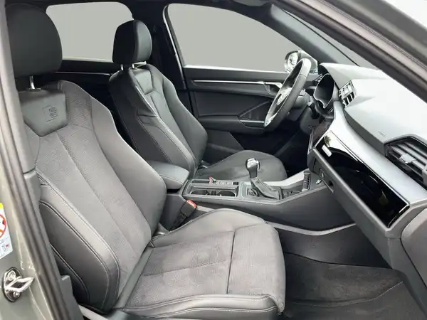 Das Bild zeigt das Innere eines AUDI Q3 mit schwarzen Sitzen und modernem Armaturenbrett.