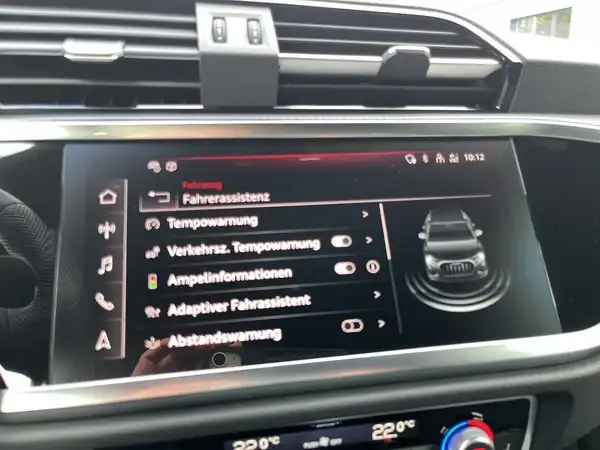 Das Bild zeigt das Innere eines AUDI Q3 mit einem Display, das verschiedene Funktionen des Fahrzeugs anzeigt, darunter Fahrassistenz und Temperaturwarnungen.