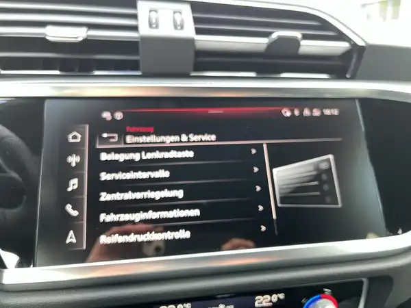 Das Bild zeigt das Inneninterieur eines AUDI Q3 mit einem Display, das Einstellungen und Serviceinformationen anzeigt. Die Innenausstattung ist schwarz.