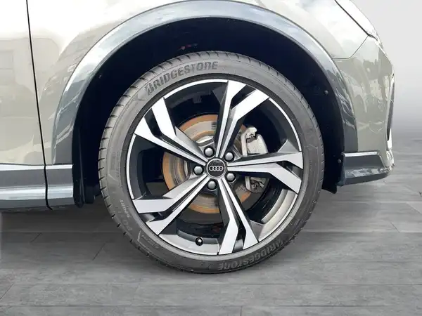 Das Bild zeigt die Seite eines Audi Q3, insbesondere das Rad und die Felge. Die Fahrzeugfarbe ist grau.