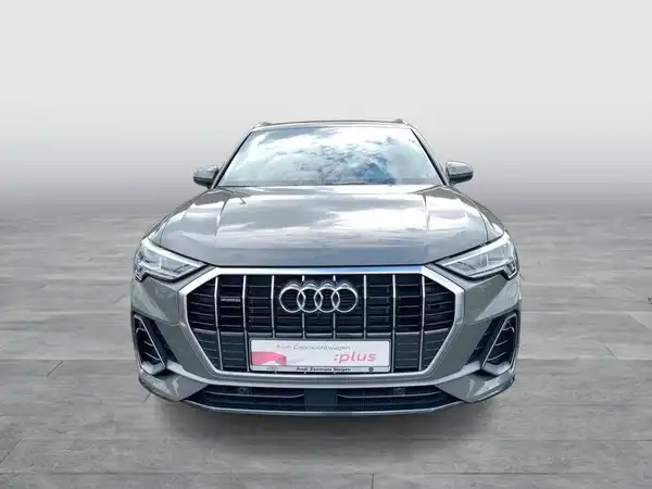 Das Bild zeigt einen grauen AUDI Q3 von vorne. Es enthält ein Händlerlogo und markante Texte.