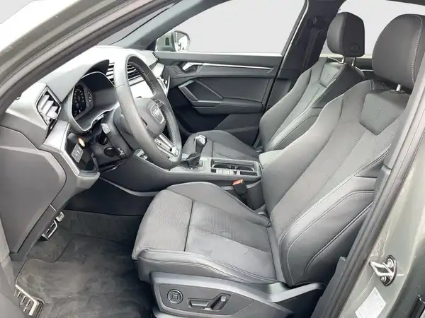 Auf dem Bild ist der Innenraum eines AUDI Q3 zu sehen, aufgenommen von der Seite. Die Sitze und das Interieur sind in schwarz.