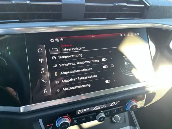 Es handelt sich um eine Innenaufnahme des Fahrzeugs, die das Infotainment-System mit verschiedenen Fahrassistenzoptionen zeigt. Der Innenraum ist schwarz.