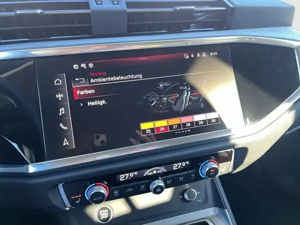 Das Bild zeigt das Innenlayout eines Audi Q3 mit dem Bildschirm, der Ambientebeleuchtung anzeigt, in einem schwarzen Innenraum.