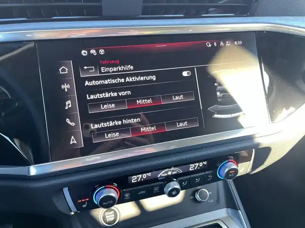 Das Bild zeigt das Innere eines AUDI Q3, speziell das Bedienfeld mit einem Infotainment-System. Die Innenfarbe ist schwarz. Es gibt mehrere Texteinblendungen auf dem Bildschirm.