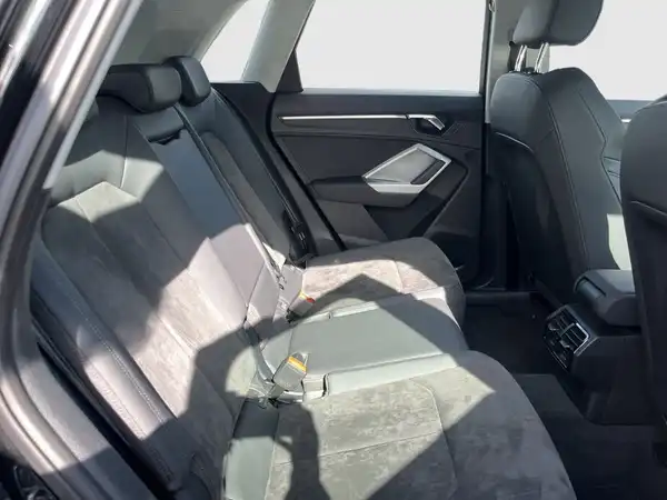 Das Bild zeigt den Innenraum eines AUDI Q3, aufgenommen von der Rückbank. Die Sitze sind schwarz und das Bild ist hell beleuchtet.