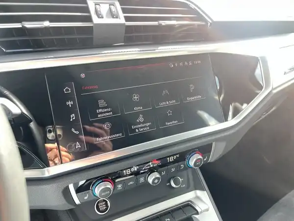 Das Bild zeigt das Innenraumdisplay eines AUDI Q3 mit verschiedenen Menüpunkten und Bedienelementen. Es handelt sich um eine Innenaufnahme des Fahrzeugs.