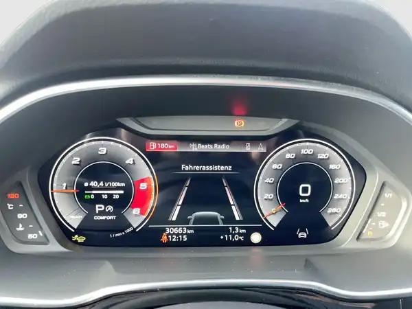 Das Bild zeigt das Armaturenbrett eines Audi Q3 mit einem digitalen Display. Die Anzeige zeigt Informationen zur Fahrassistenz und andere Fahrzeugdaten. Das Interieur ist schwarz.