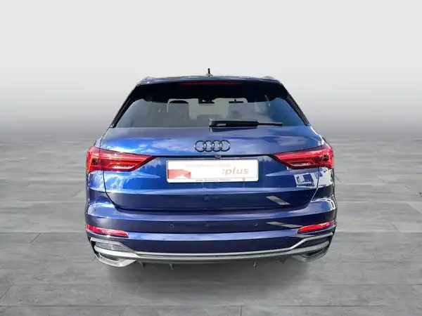 Das Bild zeigt einen blauen Audi Q3 von hinten. Es enthält das Händlerlogo und markante Texteinblendungen.
