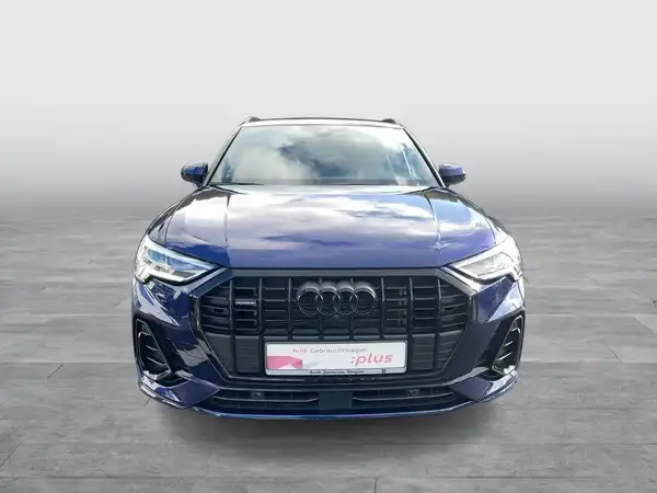 Das Bild zeigt einen blauen Audi Q3 aus der Frontansicht. Es enthält ein Händlerlogo und Text.