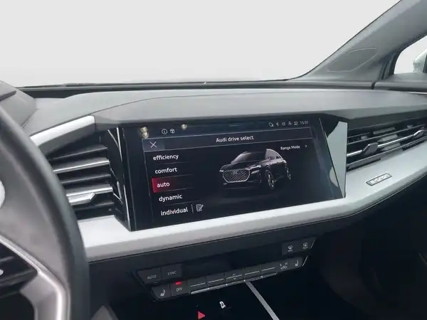 Das Bild zeigt den Innenraum eines Audi Q4 E-TRON mit einem Bildschirm, der verschiedene Fahrmodi anzeigt. Der Innenraum ist schwarz.