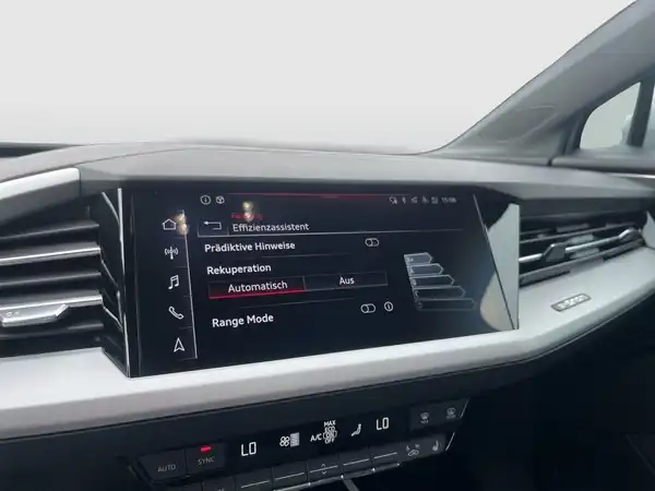 Das Bild zeigt das Innere eines AUDI Q4 E-TRON mit einem schwarzen Interieur und einem Bildschirm, der verschiedene Funktionen anzeigt.