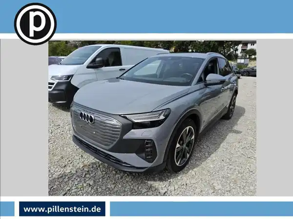 Das Bild zeigt einen grauen AUDI Q4 E-TRON aus der Frontalansicht. Im Hintergrund sind andere Fahrzeuge zu sehen und das Händlerinformationslogo ist sichtbar.