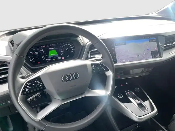 Das Bild zeigt das Innere eines AUDI Q4 SPORTBACK E-TRON mit einem schwarzen Interieur. Es enthält markante Texteinblendungen auf dem Display.