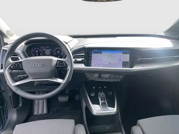 Das Bild zeigt das Innenraum eines AUDI Q4 SPORTBACK E-TRON in grauer Farbgestaltung mit einem modernen Armaturenbrett und einem Navigationssystem.