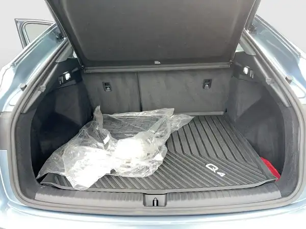 Das Bild zeigt den Kofferraum eines AUDI Q4 SPORTBACK E-TRON aus der Rückansicht. Der Innenraum ist schwarz und enthält eine Gummimatte sowie einige unidentifizierbare Gegenstände.