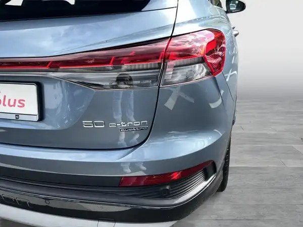 Das Bild zeigt die Rückansicht eines blauen AUDI Q4 SPORTBACK E-TRON. Es ist ein Händlerlogo sichtbar.