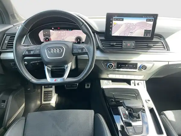 Das Bild zeigt das Innere eines AUDI Q5 mit einem schwarzen Interieur und einem Navigationssystem, das auf einer Karte zeigt.