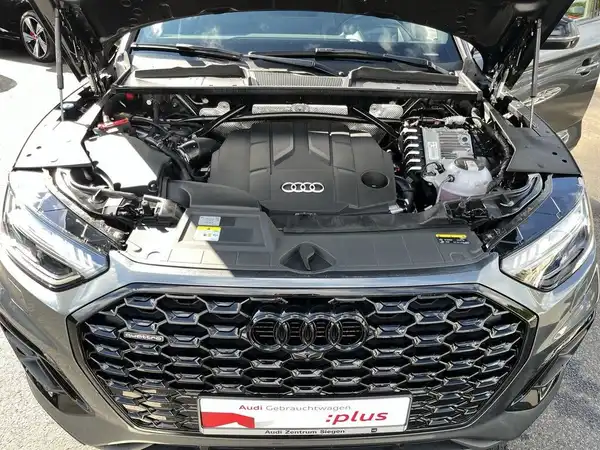 Das Bild zeigt den Motorraum eines schwarzen Audi Q5 von vorne. Das Händlerlogo ist sichtbar und es gibt markante Texteinblendungen.