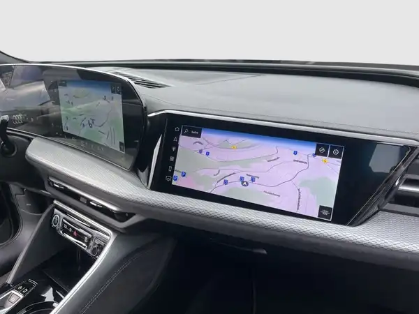 Das Bild zeigt das Innere eines Audi Q5 mit zwei Displays, die Navigationsinformationen anzeigen. Der Innenraum ist schwarz.