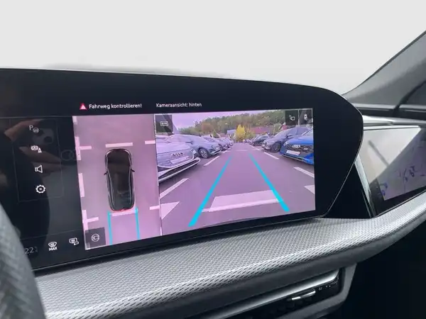 Innenaufnahme des Fahrzeugs mit einem Display, das eine Rückfahrkamera zeigt. Die Farbe des Innenraums ist schwarz und es sind markante Texteinblendungen auf dem Bildschirm zu sehen.