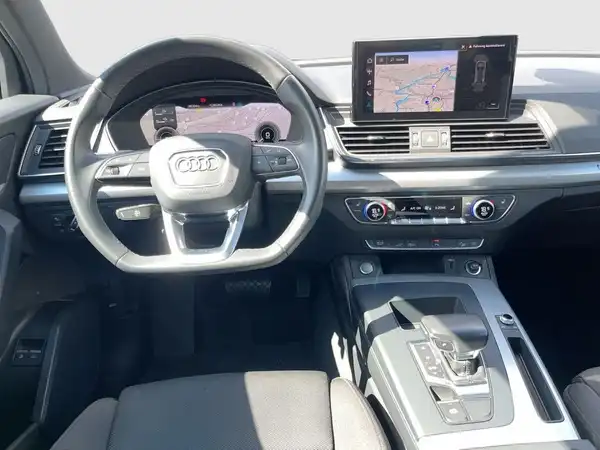 Das Bild zeigt das Innere eines AUDI Q5 von der Fahrerseite. Der Innenraum ist in Schwarz gehalten und beinhaltet ein modernes Armaturenbrett sowie ein Navigationssystem.