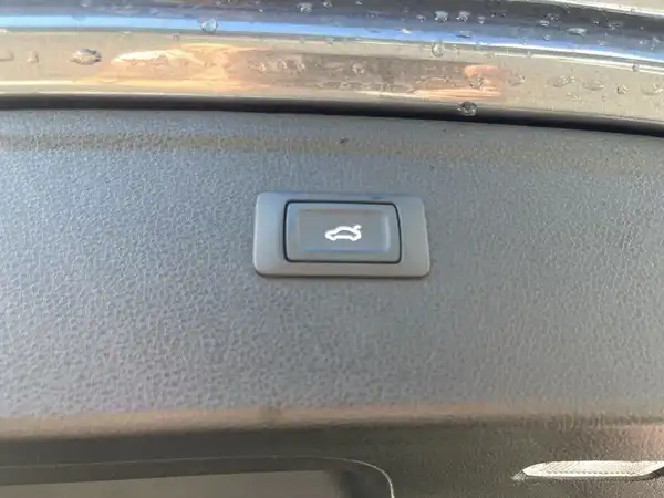 Eine Innenaufnahme des Fahrzeugs zeigt einen Knopf, wahrscheinlich für die Heckklappe, auf einem schwarzen Armaturenbrett.