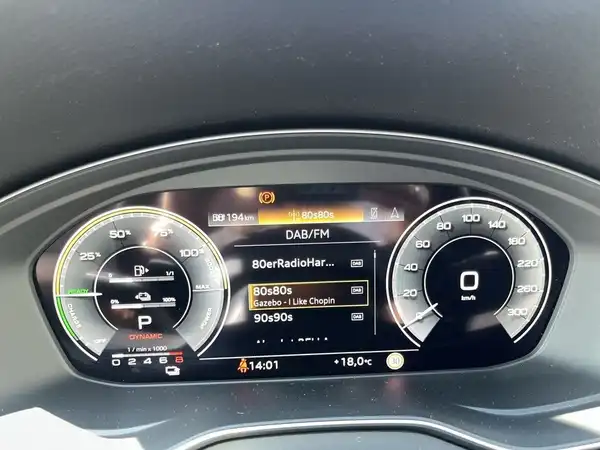 Das Bild zeigt das Armaturenbrett eines AUDI Q5 mit einem von innen aufgenommenen Bildschirm, auf dem DAB/FM-Radioinformationen angezeigt werden. Die Innenfarbe ist schwarz.