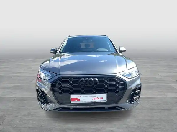 Dies ist ein Bild eines grauen AUDI Q5, aufgenommen von vorne, mit dem Händlerlogo und einer markanten Texteinblendung.