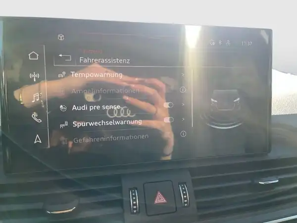 Das Bild zeigt das Innere eines Audi Q5 mit einem Bildschirm, auf dem verschiedene Funktionen wie Fahrassistentzen und Tempowarnung angezeigt werden. Es handelt sich um eine Innenaufnahme, der Innenraum ist schwarz.