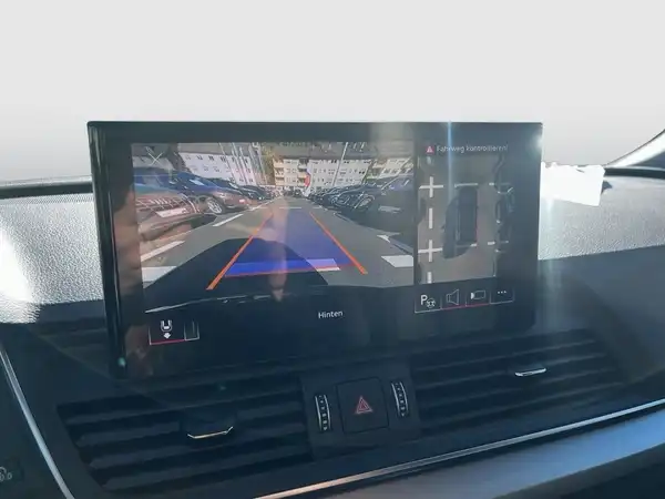 Das Bild zeigt einen Innenraum des Fahrzeugs mit einem Bildschirm, der eine Rückfahrkamera anzeigt. Das Interieur ist schwarz.